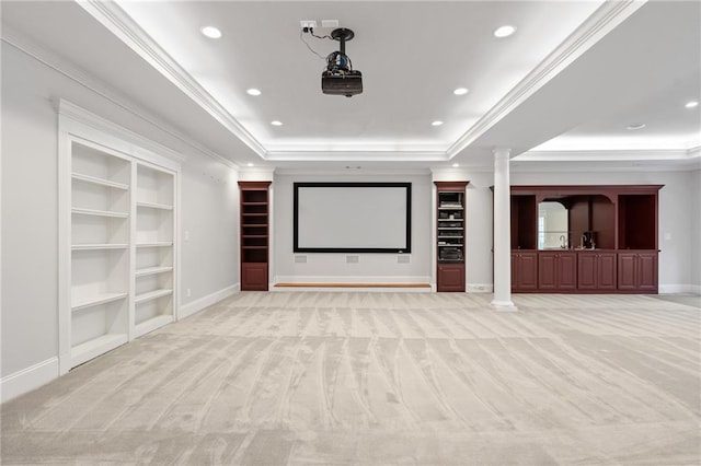 carpeted cinema featuring built in shelves, decorative columns, crown molding, and a raised ceiling