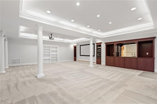 unfurnished living room featuring ornate columns, a tray ceiling, light colored carpet, and ornamental molding