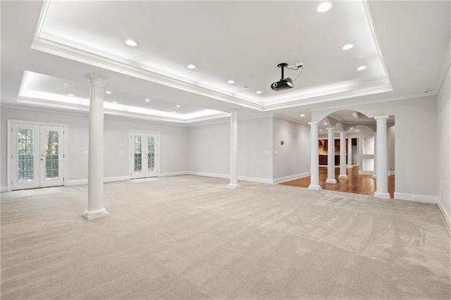 unfurnished living room with a tray ceiling, french doors, light carpet, and ornamental molding