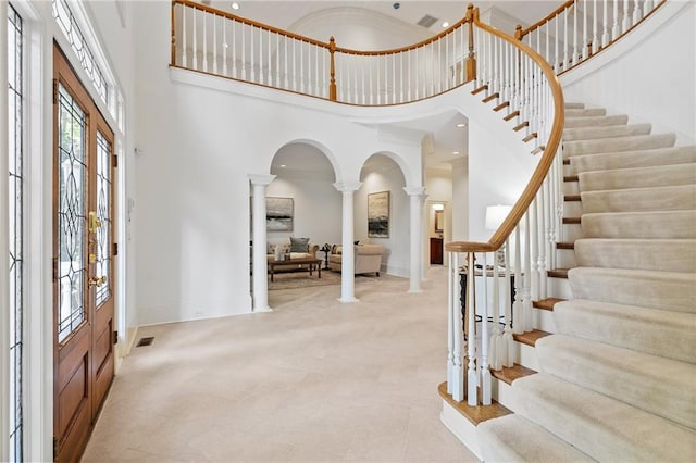 entrance foyer featuring a high ceiling, crown molding, ornate columns, and french doors