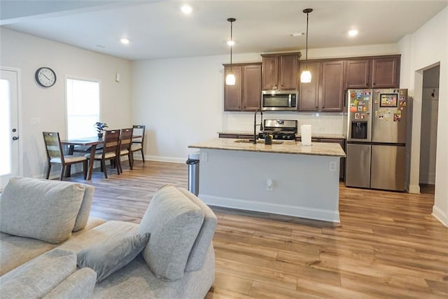 kitchen featuring light wood-style floors, open floor plan, hanging light fixtures, appliances with stainless steel finishes, and an island with sink