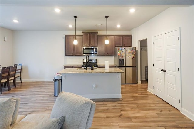 kitchen featuring a center island with sink, appliances with stainless steel finishes, hanging light fixtures, light wood-type flooring, and a sink