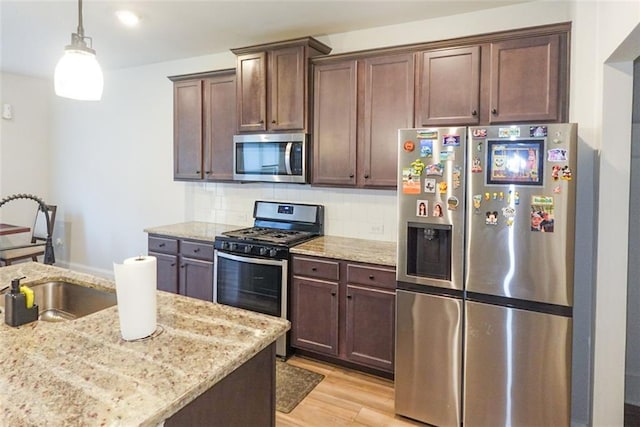 kitchen featuring stainless steel appliances, a sink, decorative light fixtures, and light stone countertops