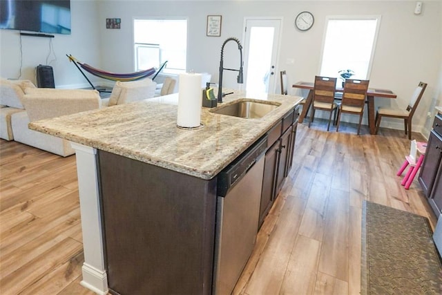 kitchen with a sink, dark brown cabinets, stainless steel dishwasher, light wood finished floors, and a center island with sink