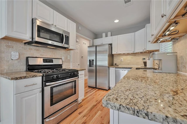 kitchen featuring tasteful backsplash, appliances with stainless steel finishes, white cabinetry, light stone counters, and light hardwood / wood-style flooring