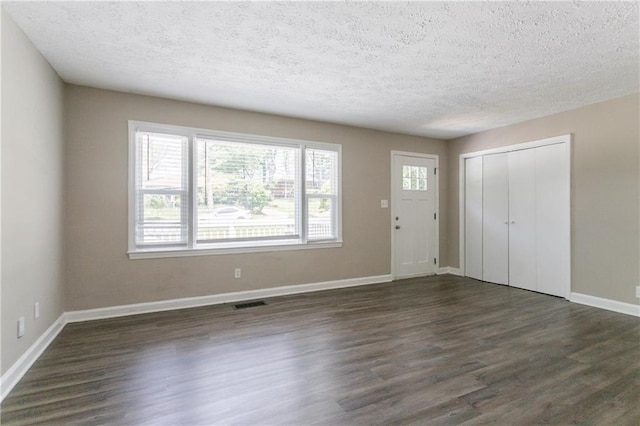 foyer featuring a textured ceiling, visible vents, baseboards, and dark wood finished floors