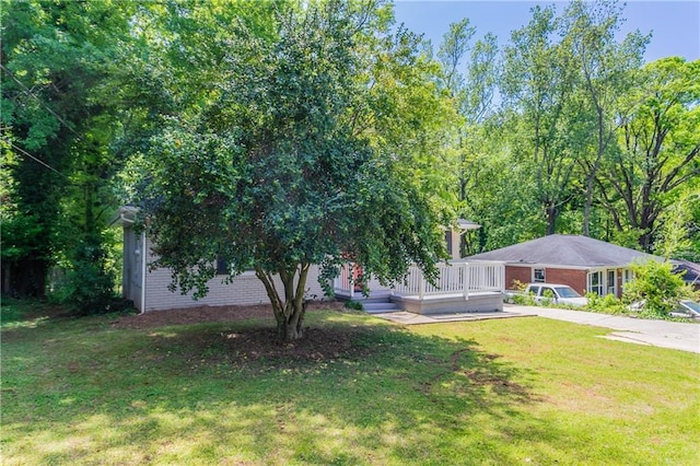 exterior space with brick siding, a wooden deck, a front yard, and driveway
