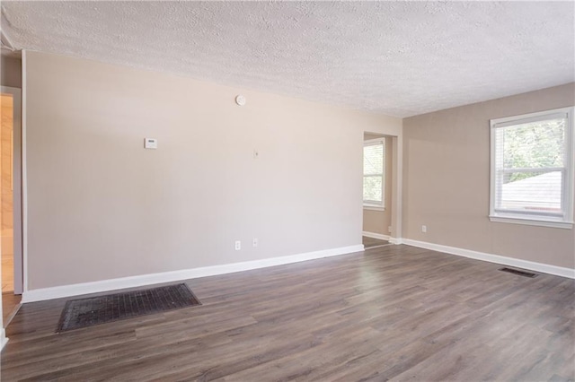empty room featuring dark wood finished floors, a wealth of natural light, and a textured ceiling