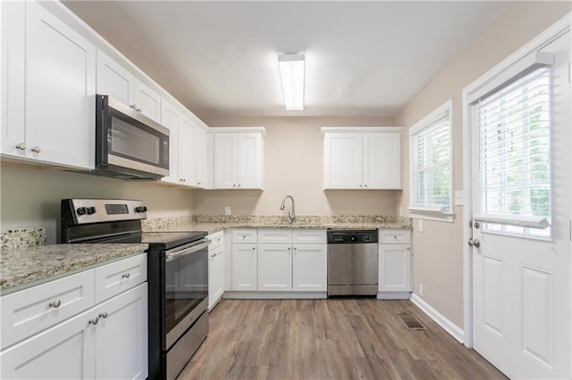 kitchen with appliances with stainless steel finishes, white cabinetry, light stone counters, and light wood-style flooring