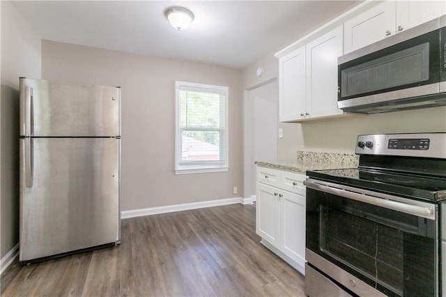 kitchen featuring appliances with stainless steel finishes, wood finished floors, white cabinetry, and baseboards