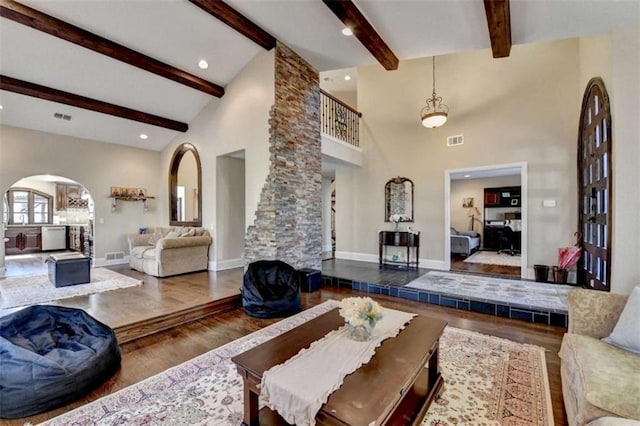 living area featuring arched walkways, high vaulted ceiling, wood finished floors, and visible vents