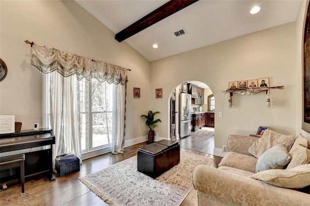 living room featuring vaulted ceiling with beams, baseboards, arched walkways, and wood finished floors