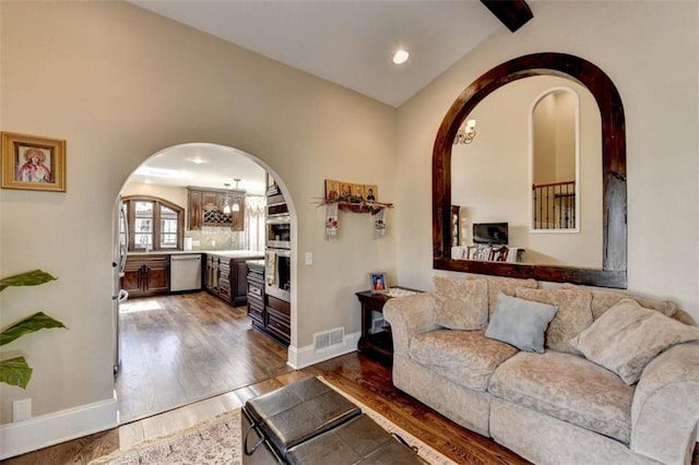 living area with dark wood-style floors, arched walkways, lofted ceiling, visible vents, and baseboards