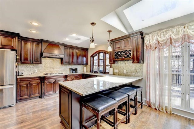 kitchen with pendant lighting, stainless steel appliances, premium range hood, a peninsula, and a kitchen breakfast bar