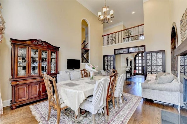 dining space featuring arched walkways, light wood finished floors, a high ceiling, a chandelier, and baseboards