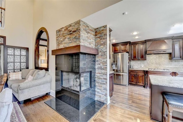 living area with a stone fireplace, recessed lighting, a high ceiling, and light wood-style floors