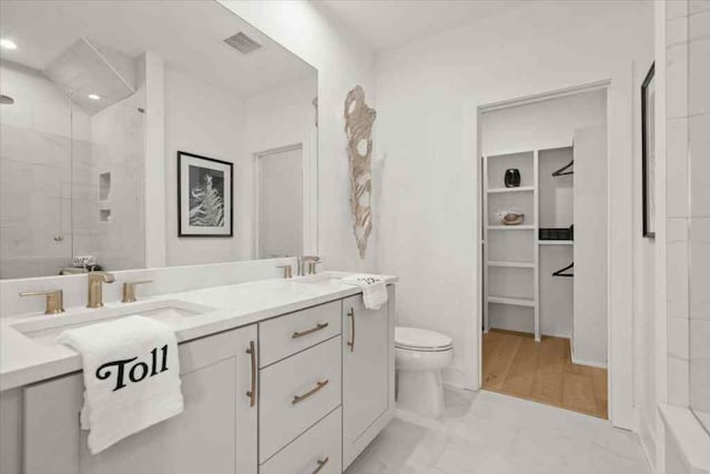 bathroom with toilet, double vanity, a shower stall, and a spacious closet