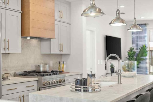 kitchen with high end range, light stone countertops, hanging light fixtures, a kitchen island with sink, and backsplash