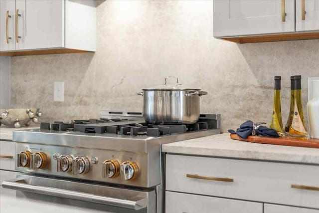 kitchen with high end stainless steel range, white cabinets, light stone countertops, and tasteful backsplash