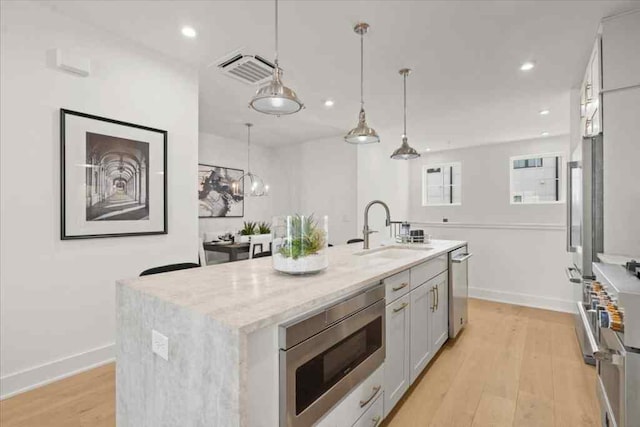 kitchen featuring light stone countertops, light wood-style floors, appliances with stainless steel finishes, a sink, and pendant lighting