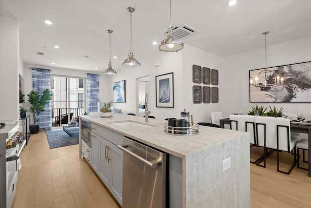 kitchen with stainless steel dishwasher, a sink, an inviting chandelier, open floor plan, and light stone countertops