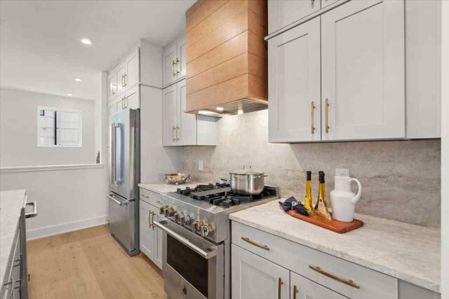 kitchen with tasteful backsplash, light wood-style flooring, premium appliances, premium range hood, and recessed lighting