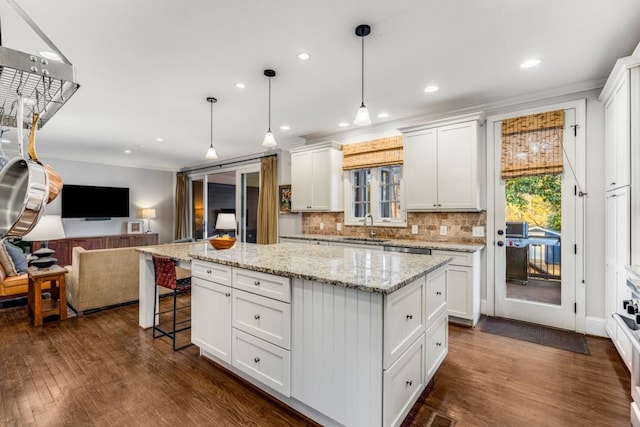 kitchen with a kitchen island, white cabinetry, sink, hanging light fixtures, and light stone countertops