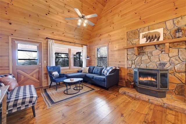 living room featuring wooden walls, wood-type flooring, ceiling fan, a fireplace, and high vaulted ceiling