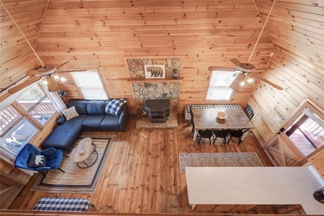 unfurnished living room with a stone fireplace, wood finished floors, a ceiling fan, and wooden walls