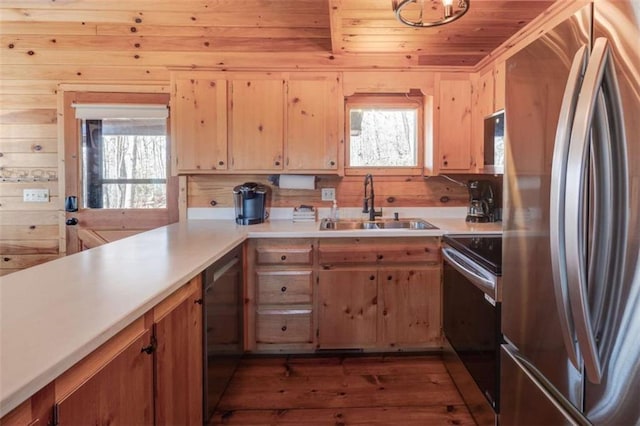 kitchen featuring dark wood-style flooring, stainless steel appliances, light countertops, wood walls, and a sink