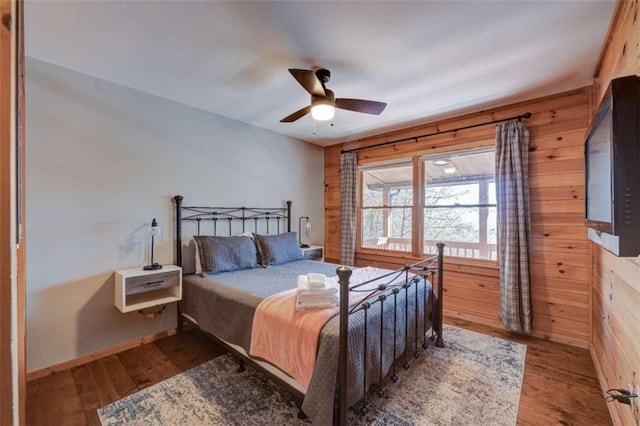 bedroom with a ceiling fan, wooden walls, and hardwood / wood-style floors