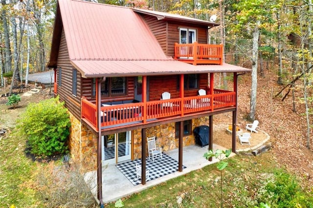 rear view of property featuring a patio, metal roof, a balcony, stone siding, and log veneer siding