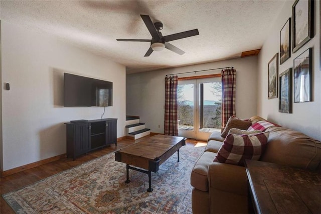 living area with a textured ceiling, wood finished floors, a ceiling fan, baseboards, and stairway