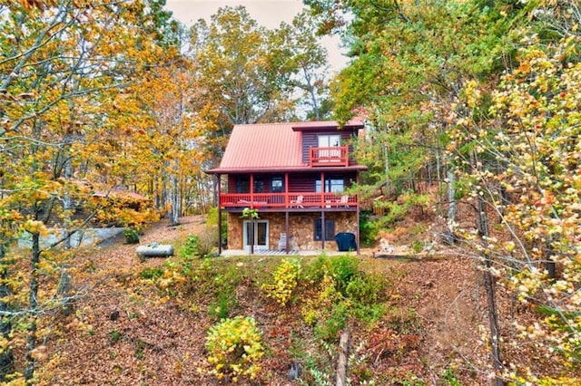 rear view of property featuring stone siding, a deck, and metal roof