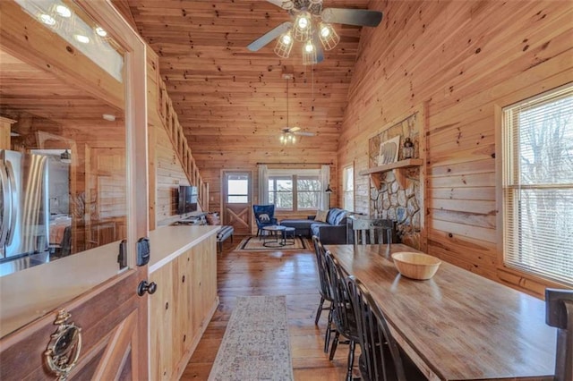 dining space featuring high vaulted ceiling, wood finished floors, a ceiling fan, and wooden walls