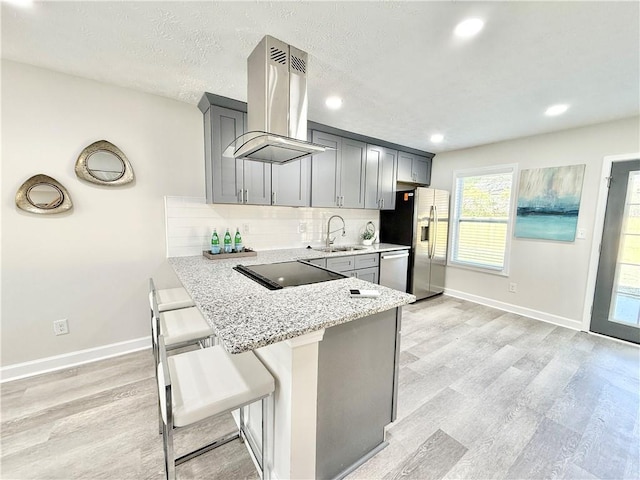 kitchen featuring decorative backsplash, appliances with stainless steel finishes, island exhaust hood, gray cabinets, and a sink