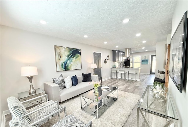 living room with recessed lighting, baseboards, a textured ceiling, and light wood finished floors