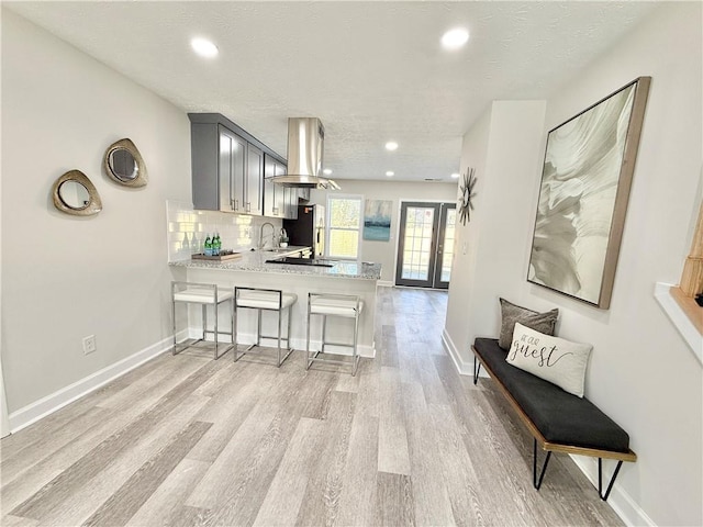 kitchen featuring tasteful backsplash, a peninsula, island exhaust hood, light countertops, and light wood-type flooring