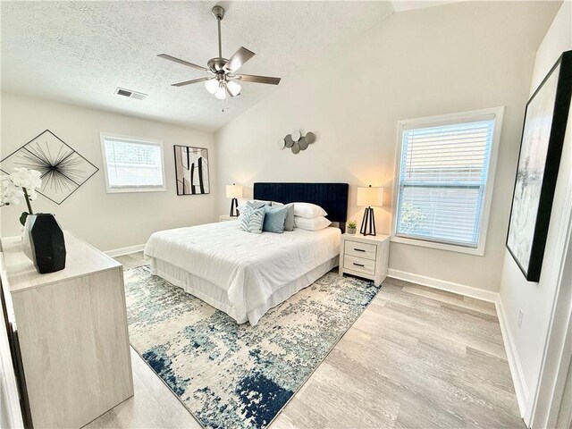 bedroom featuring light wood-type flooring, visible vents, vaulted ceiling, and a textured ceiling