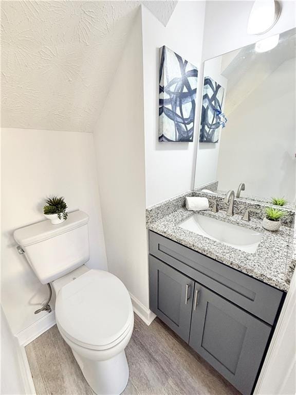 half bathroom with a textured ceiling, toilet, wood finished floors, vanity, and vaulted ceiling