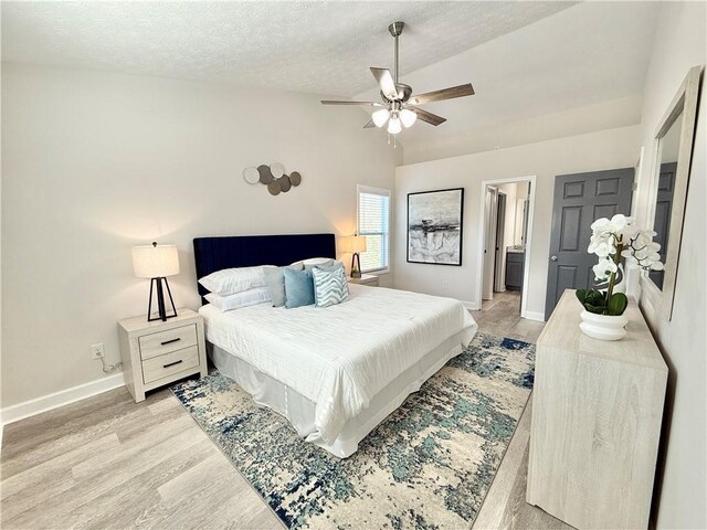 bedroom with a textured ceiling, lofted ceiling, light wood-style flooring, and baseboards