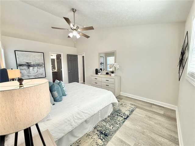 bedroom with a textured ceiling, lofted ceiling, a ceiling fan, baseboards, and light wood-type flooring