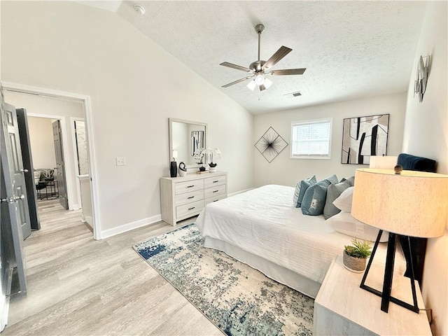 bedroom featuring light wood finished floors, baseboards, visible vents, vaulted ceiling, and a textured ceiling