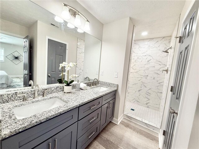 ensuite bathroom featuring a textured ceiling, wood finished floors, a sink, and visible vents