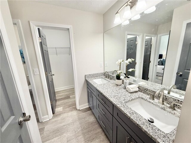 full bath featuring double vanity, a textured ceiling, a sink, and wood finished floors