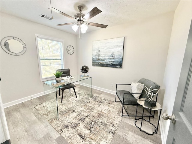 home office featuring a textured ceiling, wood finished floors, a ceiling fan, visible vents, and baseboards