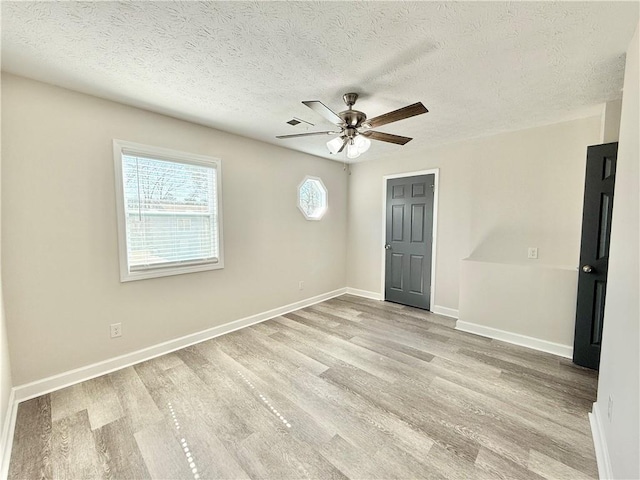 empty room with visible vents, ceiling fan, a textured ceiling, wood finished floors, and baseboards