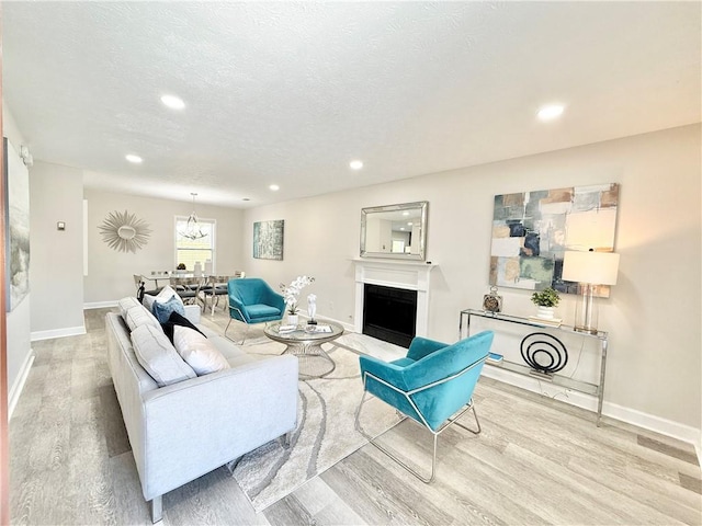 living area with baseboards, a fireplace, a textured ceiling, and light wood finished floors