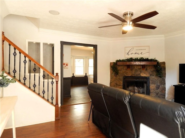 living room featuring crown molding, wood finished floors, ceiling fan, stairway, and a stone fireplace