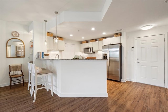 kitchen with dark stone countertops, appliances with stainless steel finishes, kitchen peninsula, pendant lighting, and white cabinets